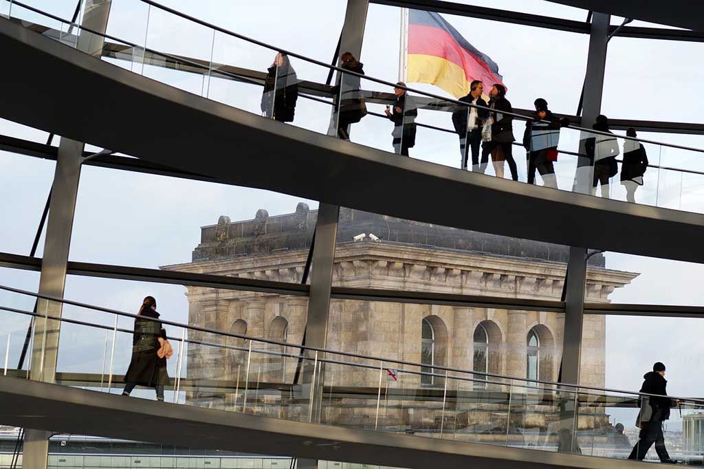 Les visiteurs déambulent sur les rampes en spirale à l'intérieur du dôme de verre du Bundestag allemand, sous le drapeau allemand.