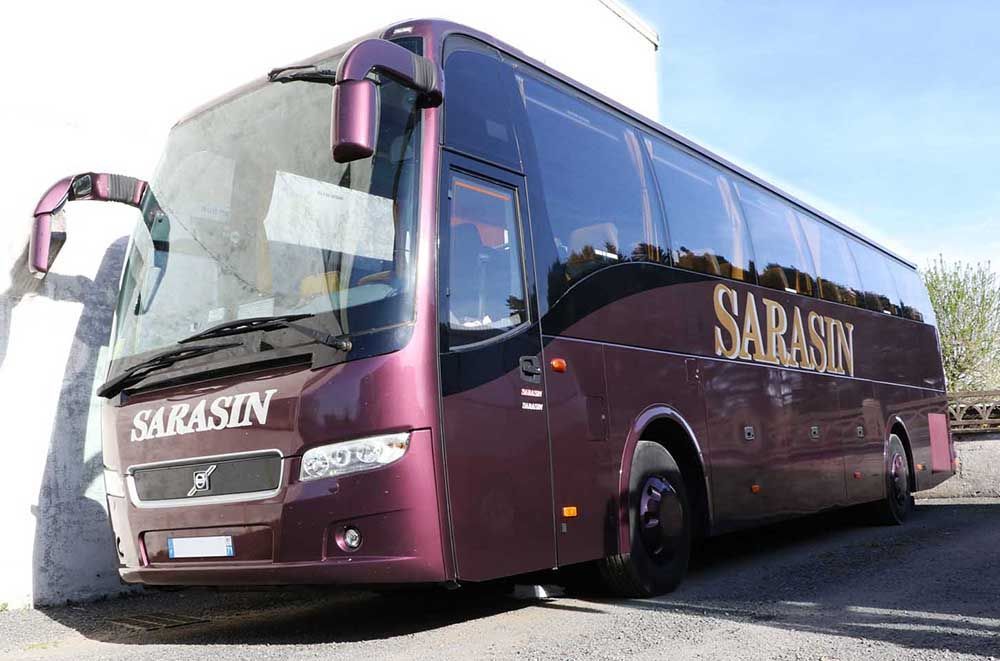 Un autocar Sarasin violet garé contre un mur blanc par une journée ensoleillée.