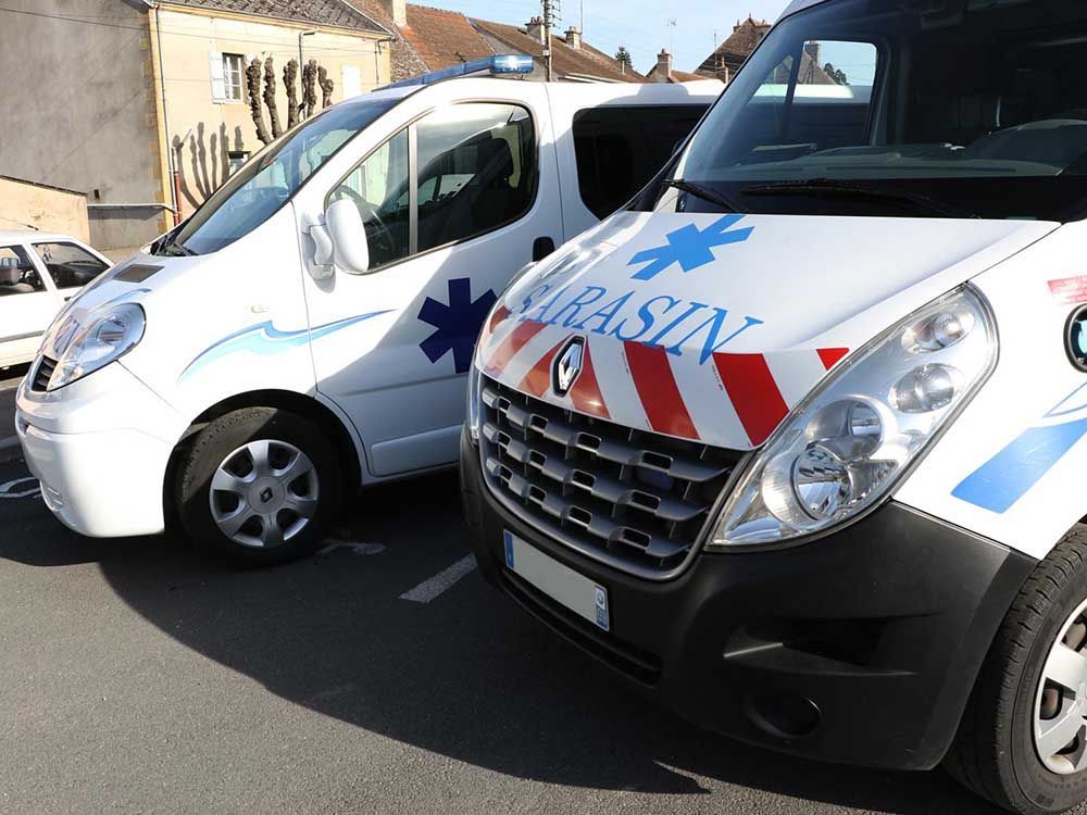 Deux ambulances blanches arborant le symbole de l'étoile de vie et l'inscription SARASIN sont stationnées sur un parking asphalté.