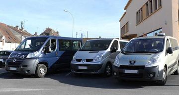 Trois fourgonnettes, de couleur bleue, argentée et grise, étaient garées côte à côte devant un bâtiment par une journée ensoleillée.