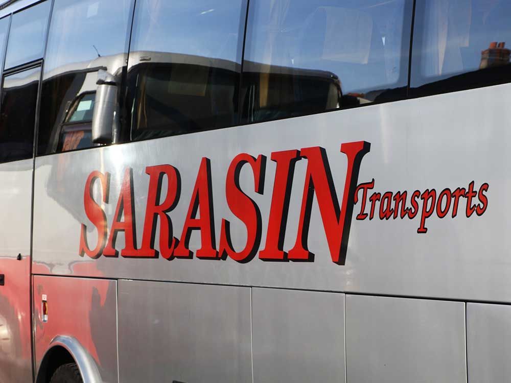 Gros plan latéral d'un bus argenté avec l'inscription rouge SARASIN Transports.
