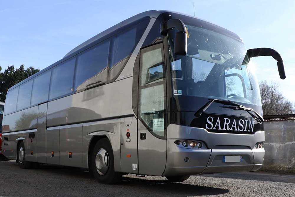Un autocar de tourisme argenté portant l'inscription SARASIN à l'avant, stationné à l'extérieur par une journée ensoleillée.
