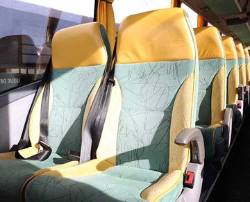 Des rangées de sièges de bus vides, avec des appuie-têtes jaunes et des coussins turquoise à motifs, dans l'habitacle d'un véhicule baigné de lumière.