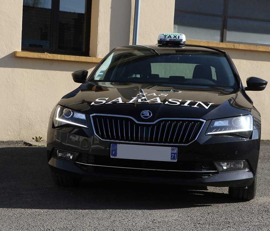 Un taxi Skoda noir garé devant un immeuble, avec l'inscription SARASIN sur son capot.