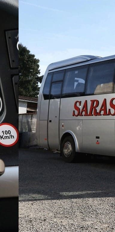 Un bus argenté portant l'inscription SARASIN sur le côté, vu à travers un cadre sombre affichant un panneau de limitation de vitesse à « 100 km/h ».