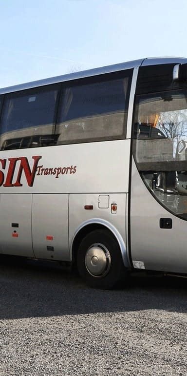 Un autocar argenté de tourisme est stationné à l'extérieur avec l'inscription SARASIN Transports sur le côté.
