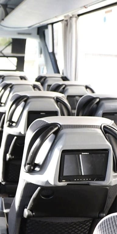 Des rangées de sièges passagers gris à l'intérieur d'un bus, chacun équipé d'un écran intégré à l'appui-tête.