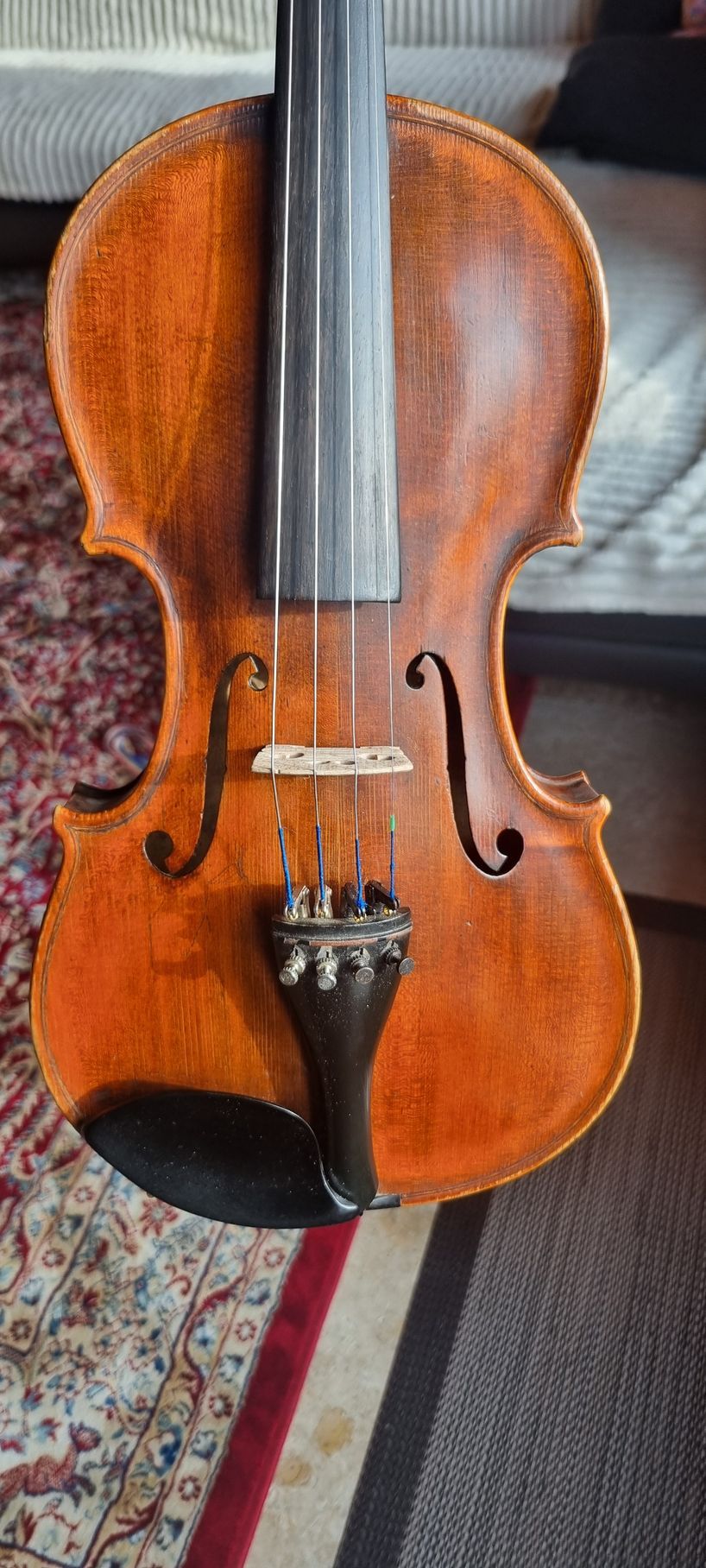Gros plan sur un violon marron, dont on aperçoit les cordes et le chevalet, sur un tapis à motifs.