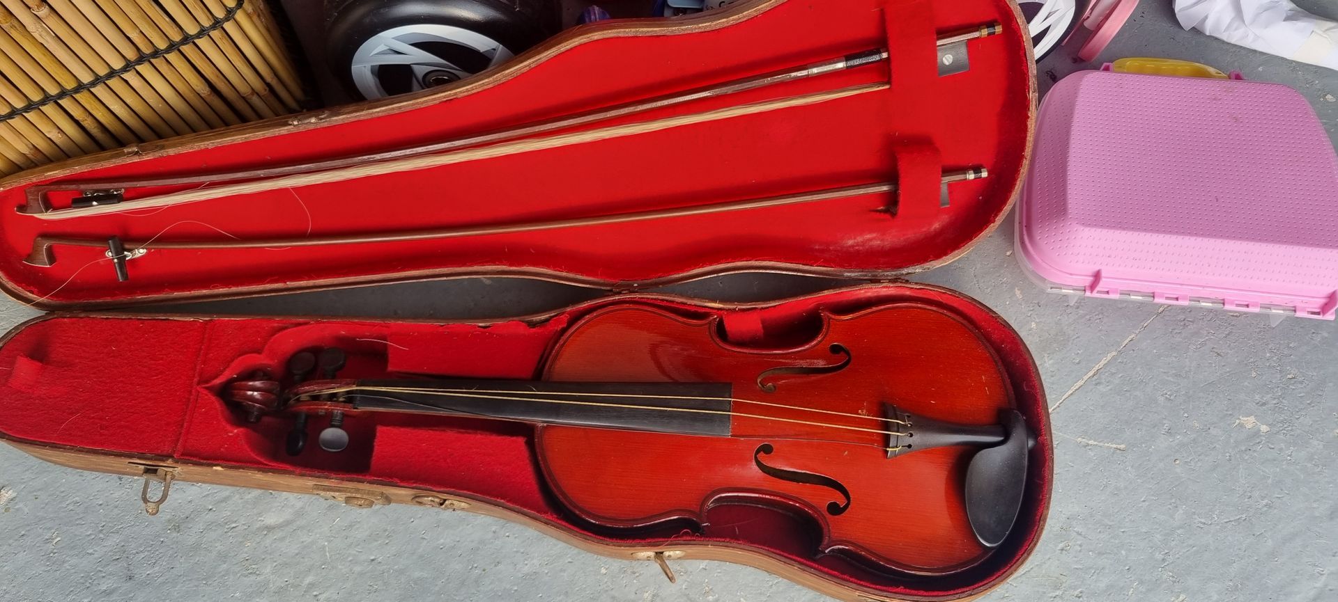 Étui à violon ouvert contenant un violon et deux archets, à côté d'un étui rose.