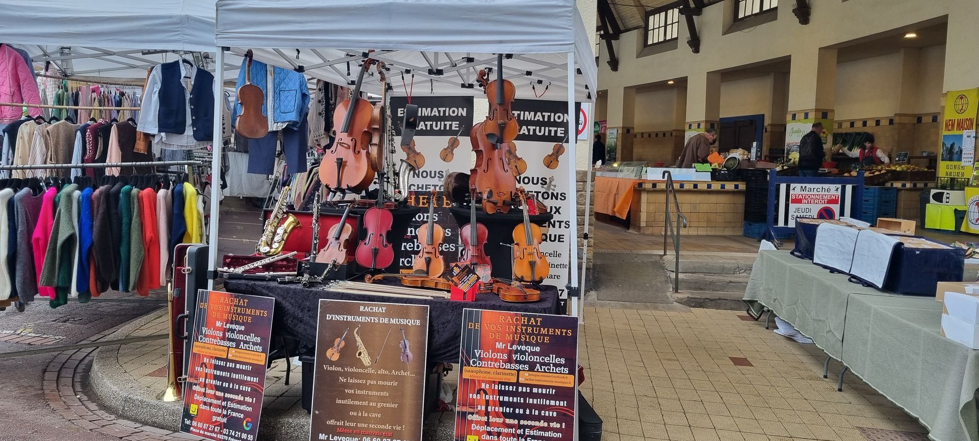 Étal de présentant des violons et annonçant une estimation gratuite. Auvent blanc, sol pavé.