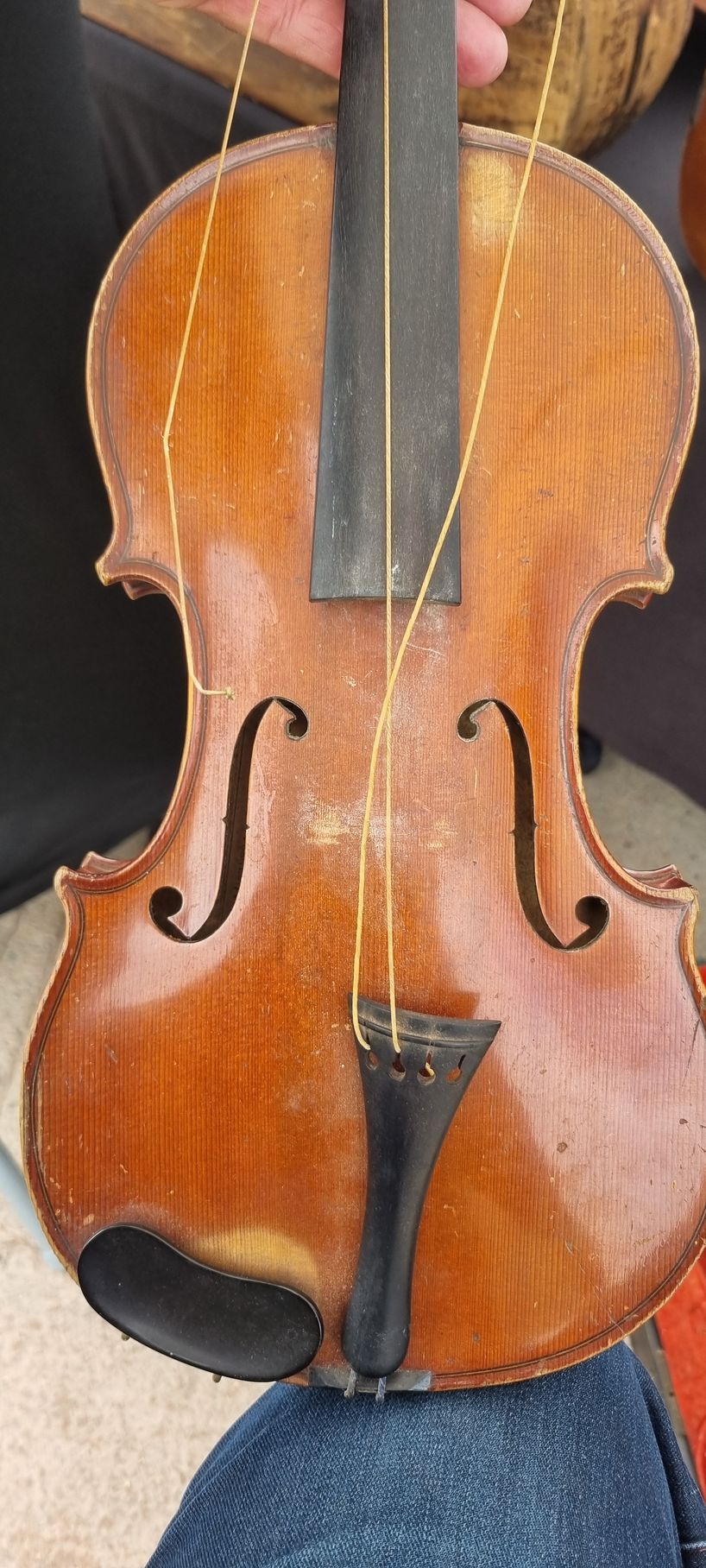 Un violon, tenu à deux mains, repose sur du denim. L'instrument est brun avec des accents noirs et des cordes dorées.