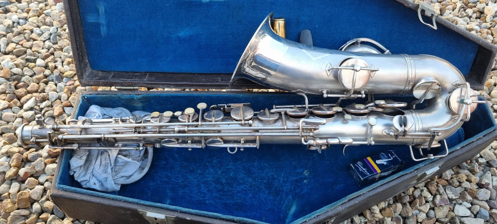 Saxophone argenté dans un étui bleu, en extérieur.