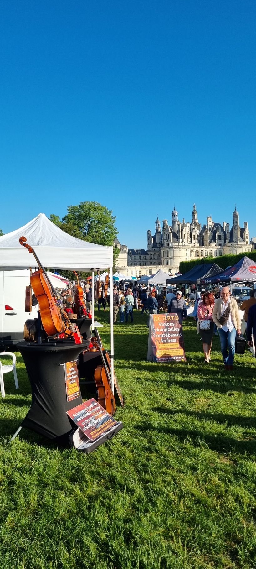 Événement en plein air avec un violon exposé, un château en arrière-plan, ciel bleu.