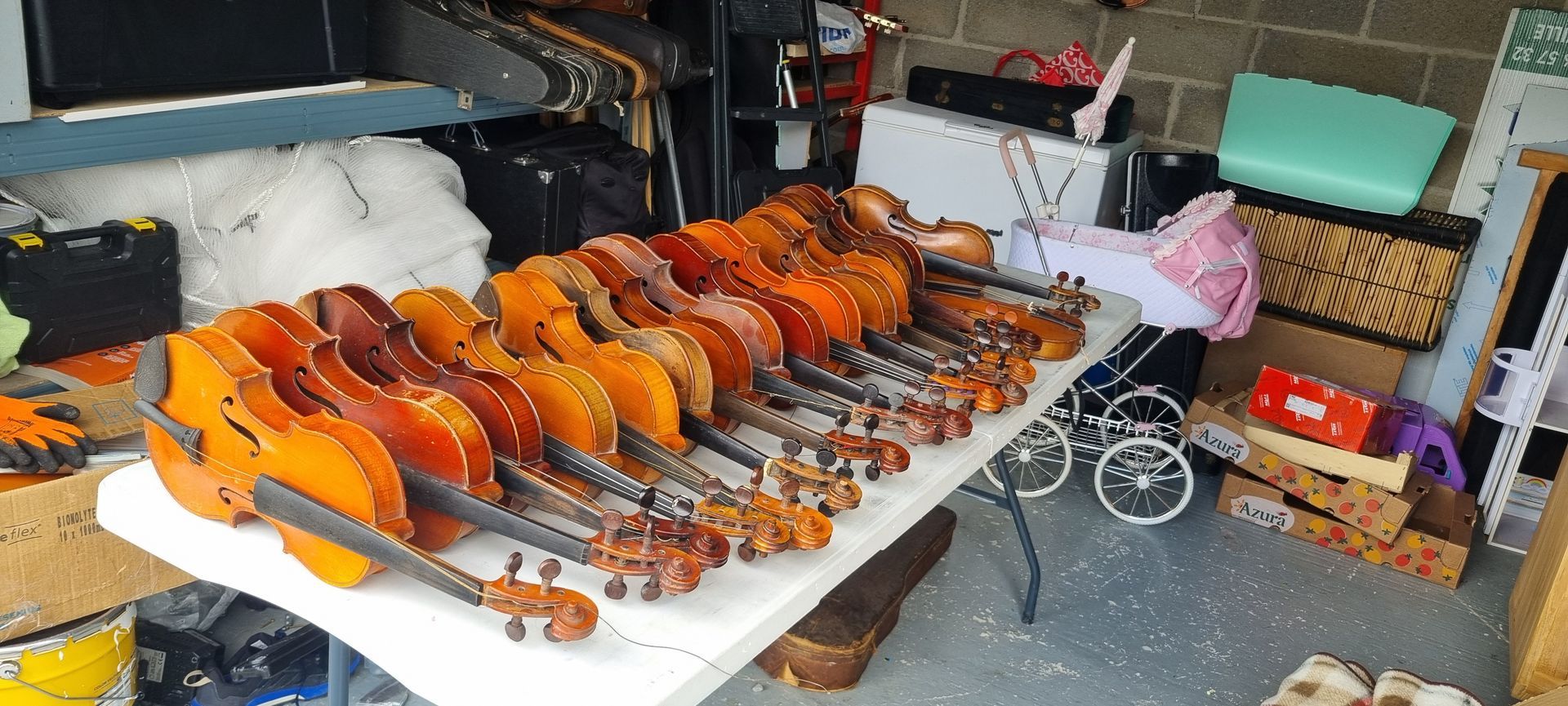 Une collection de violons exposée sur une table blanche dans un garage encombré.