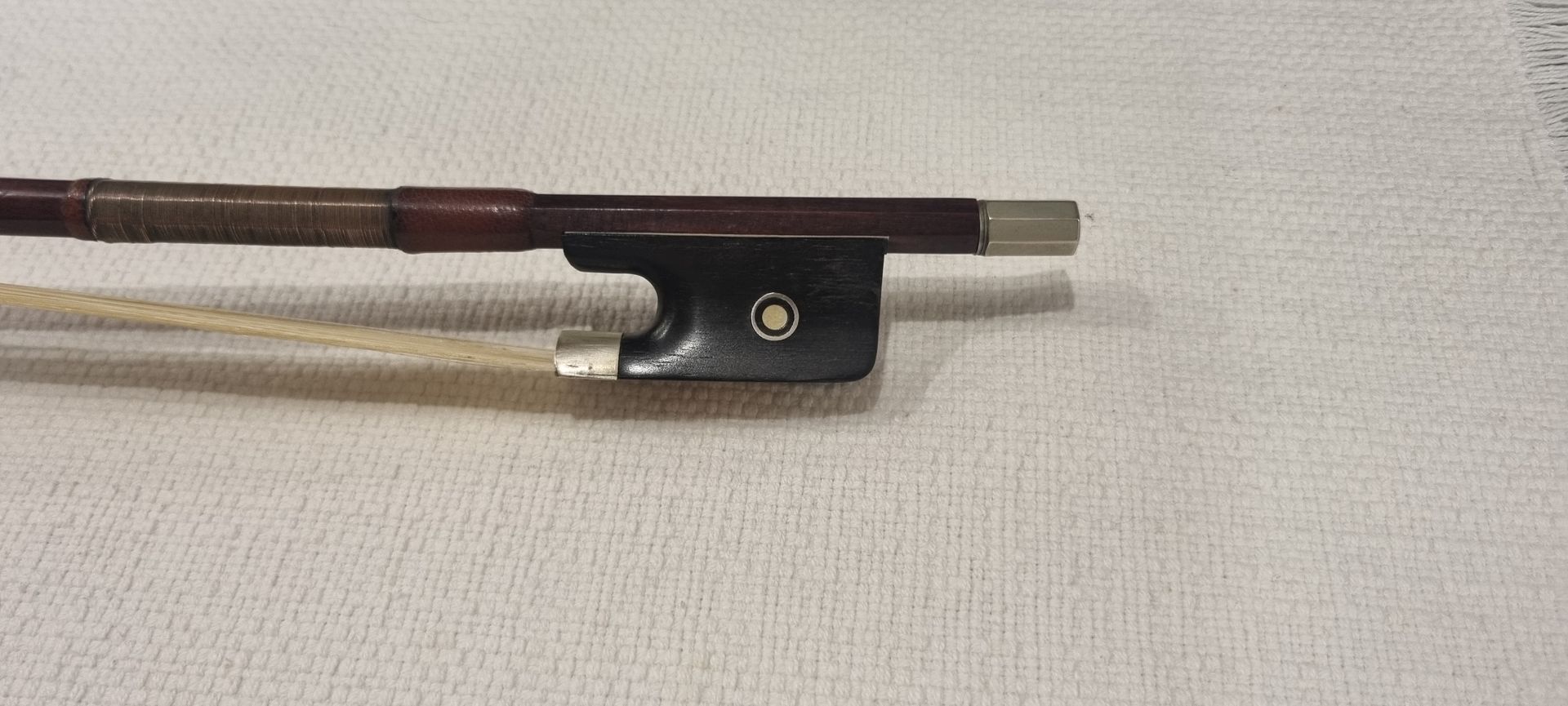 Gros plan sur un archet de violon posé sur une surface texturée de couleur claire.