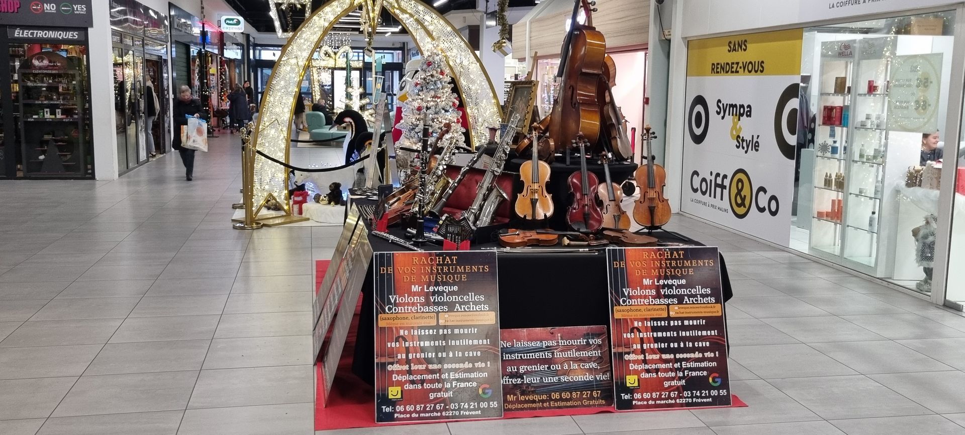 Des instruments de musique sont exposés dans un centre commercial sous une arche. Des passants déambulent.