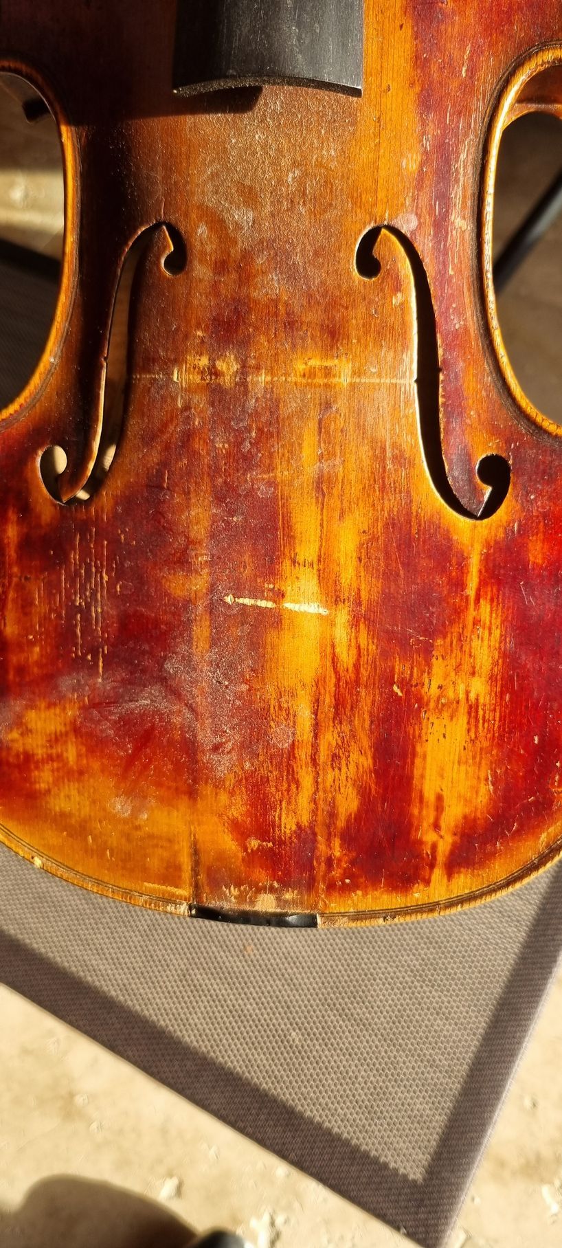 Gros plan sur la table d'un violon ancien et usé, montrant un bois vieilli aux tons rougeâtres et dorés, une ombre visible.