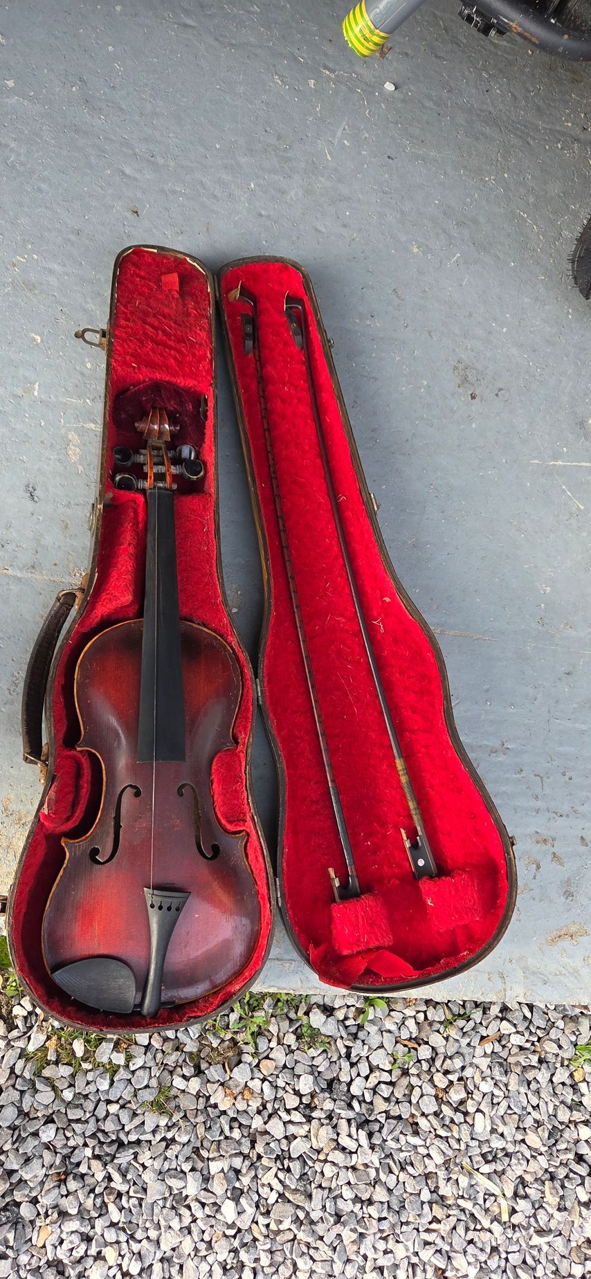 Un violon brun dans un étui ouvert doublé de velours rouge, posé sur une surface grise.