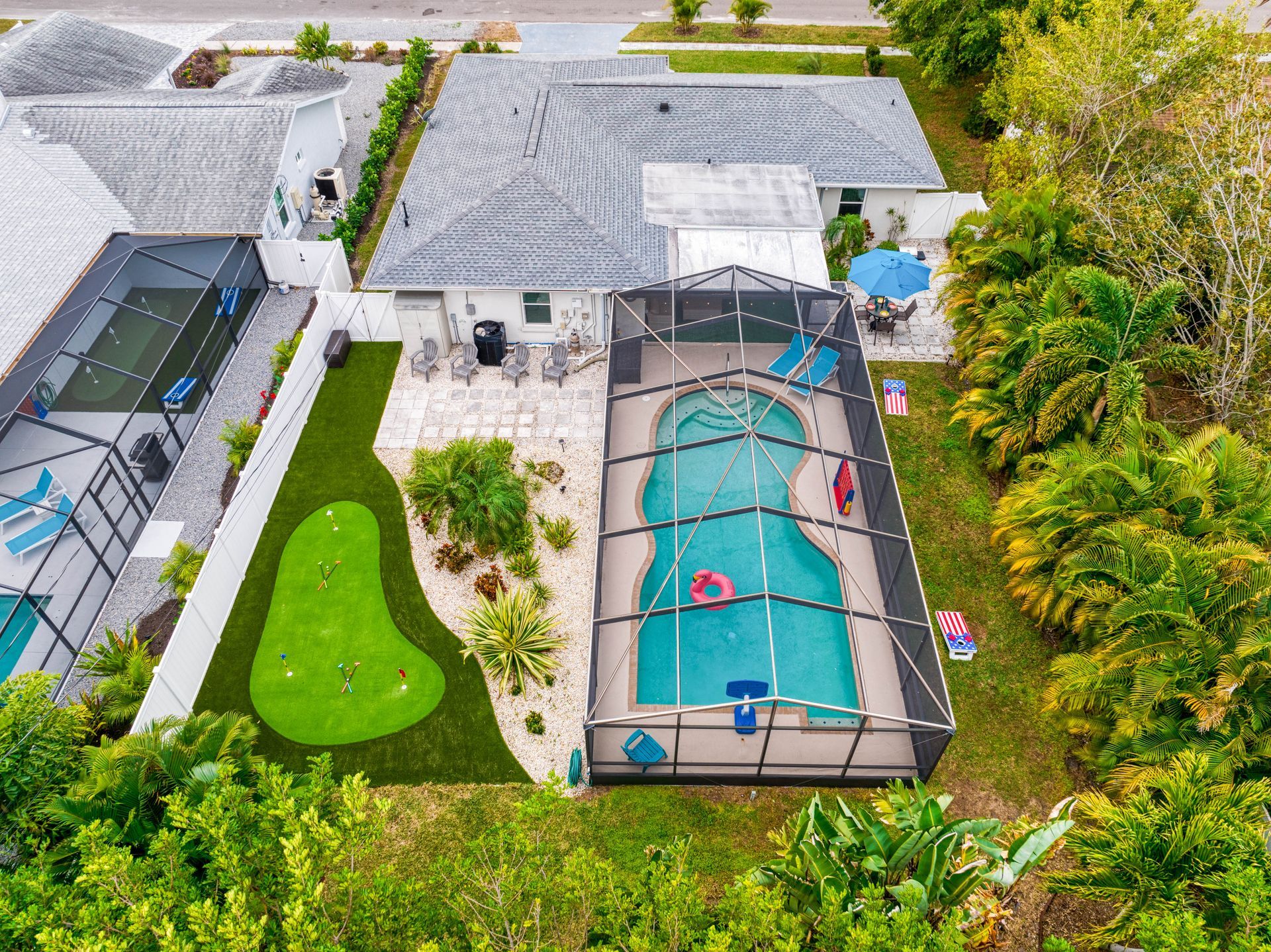 Aerial view of a house with a pool, putting green, and lush landscaping in a sunny setting.