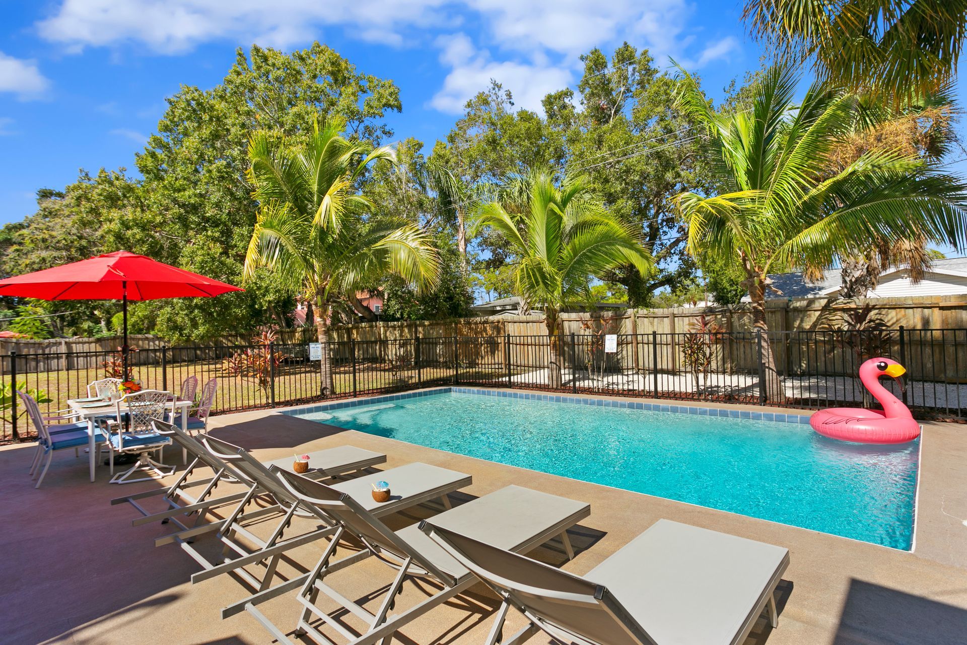 Swimming pool with lounge chairs, red umbrella, and pink flamingo floatie.