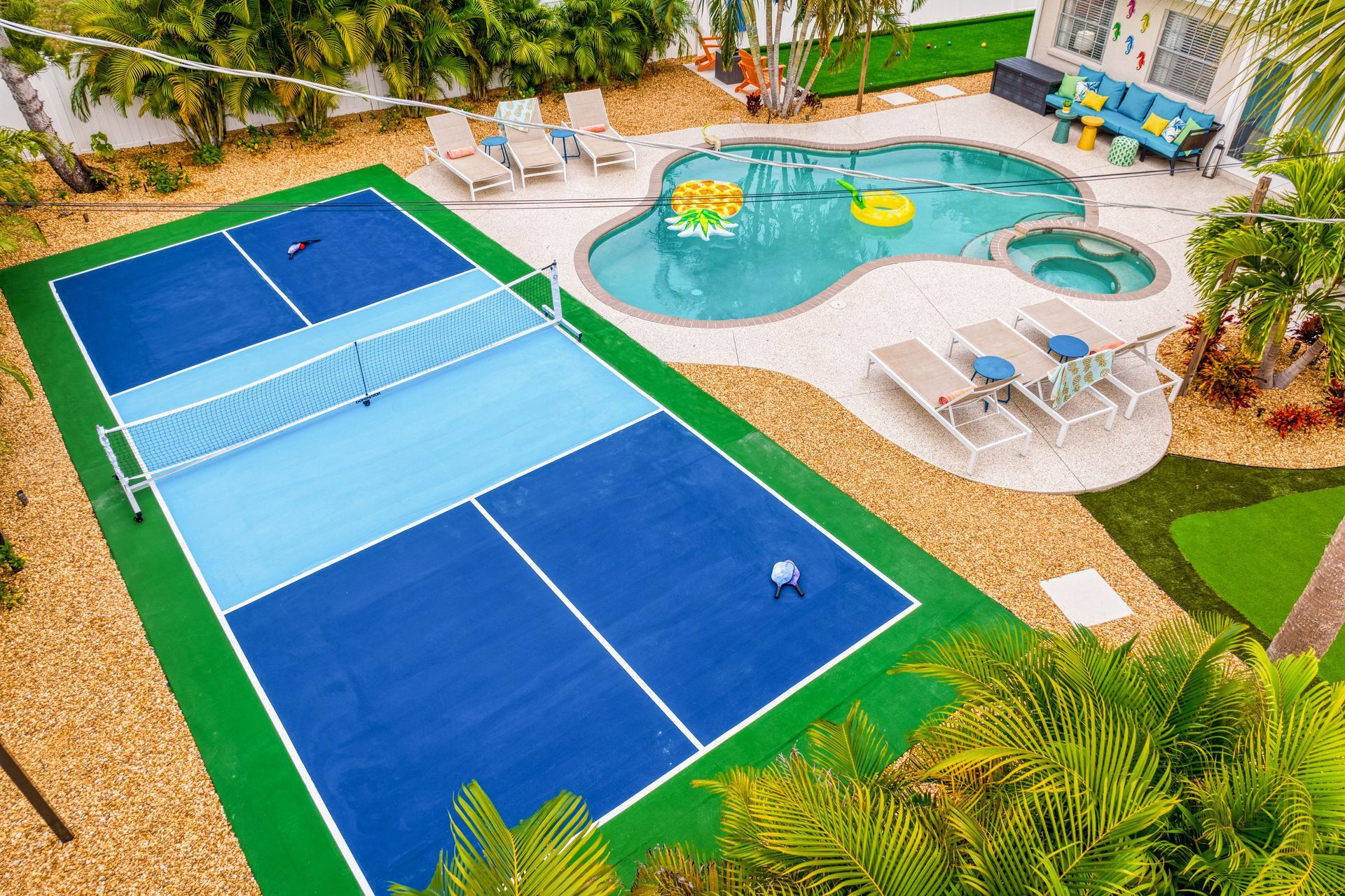 Overhead view of a backyard with a pickleball court, swimming pool, and lounge area.