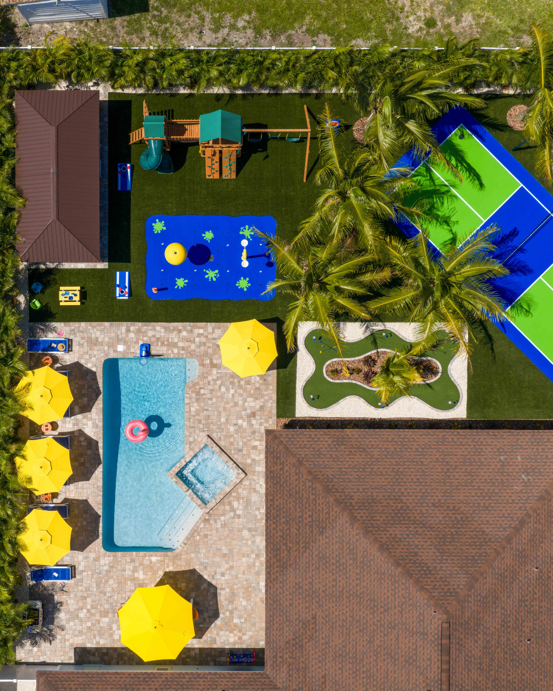 Aerial view of a luxurious backyard with pool, playground, and tennis court; yellow umbrellas and 