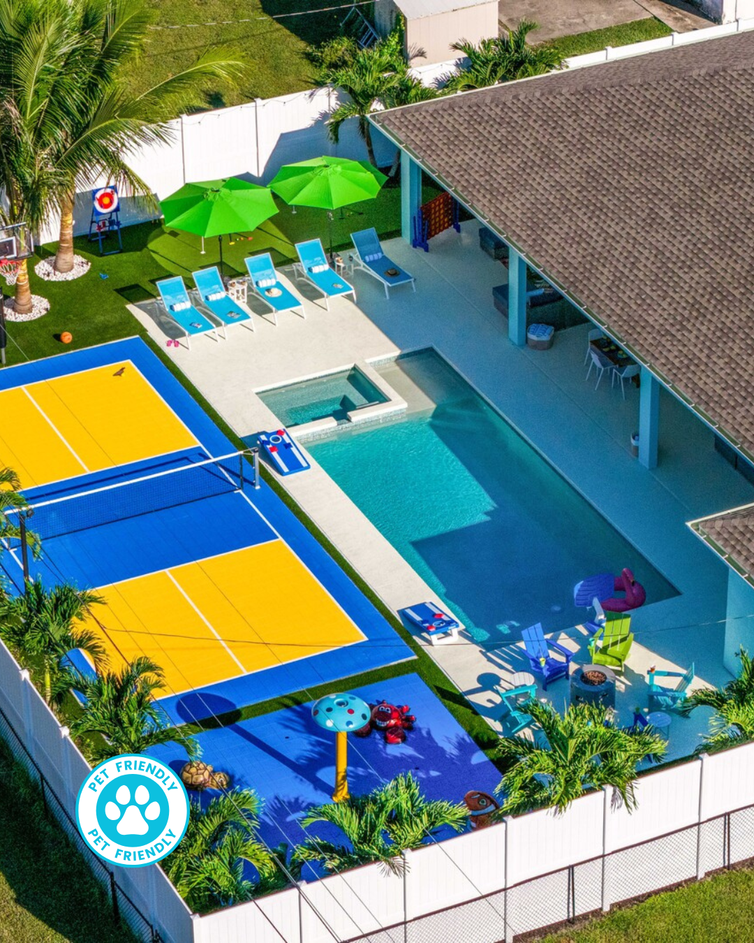 Poolside patio with a dining table, chairs, and outdoor grill. Blue pool and lounge chairs, lush greenery in the background.
