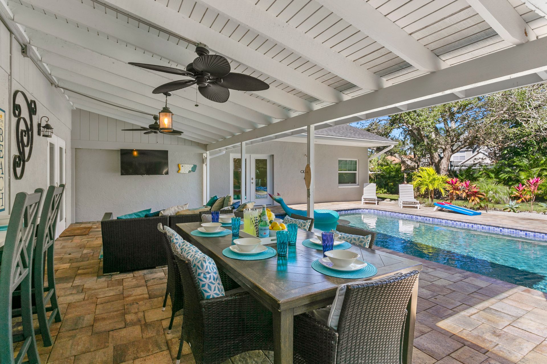 Patio with table set for dining, overlooking a pool. Blue and white decor, a ceiling fan, and green yard.