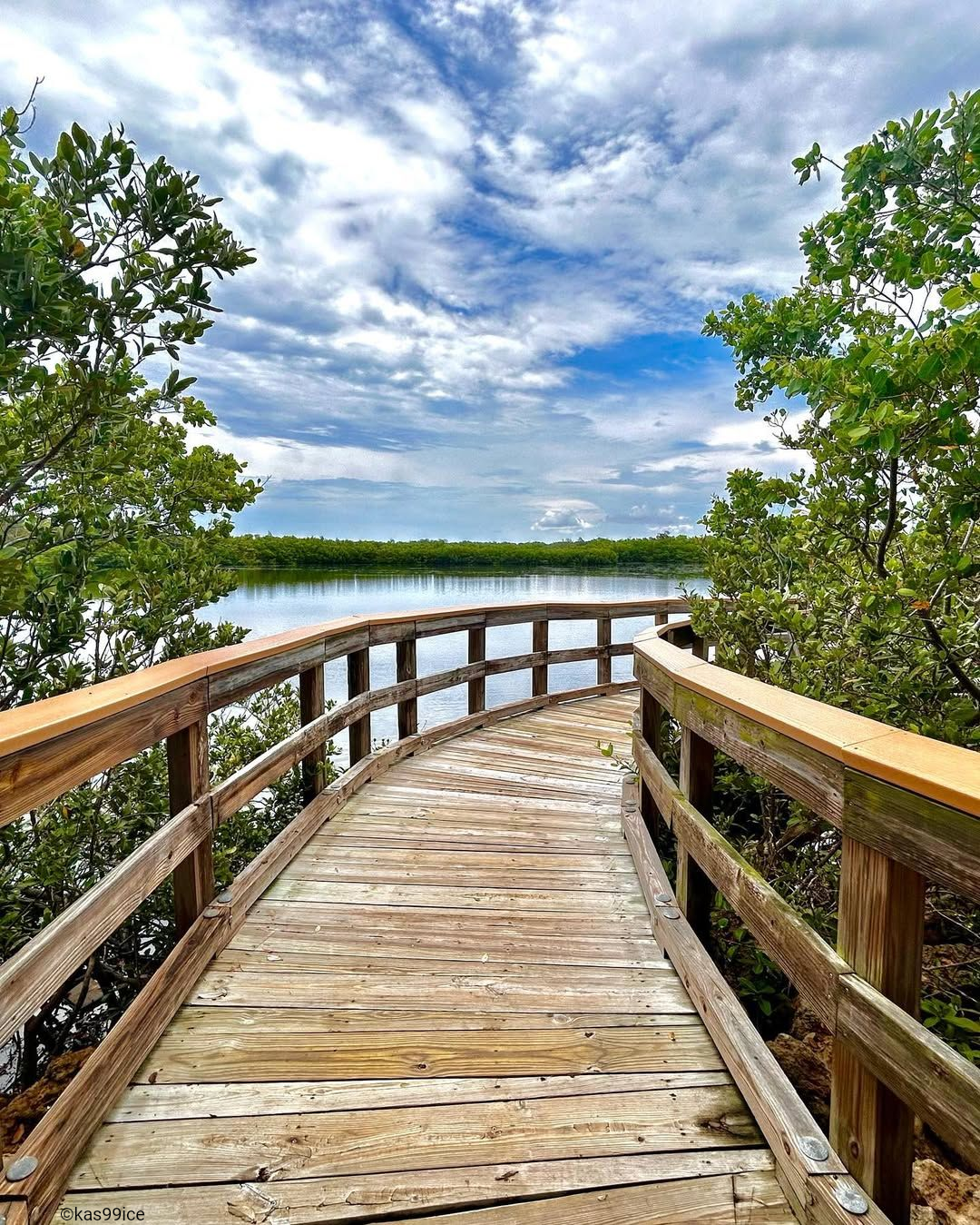 Wooden pier extending toward the sunrise over calm water, benches on either side.