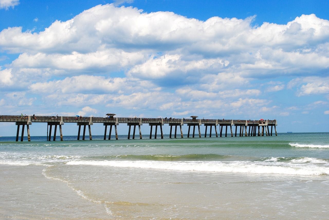 Long pier over shallow ocean under a bright blue sky with scattered clouds