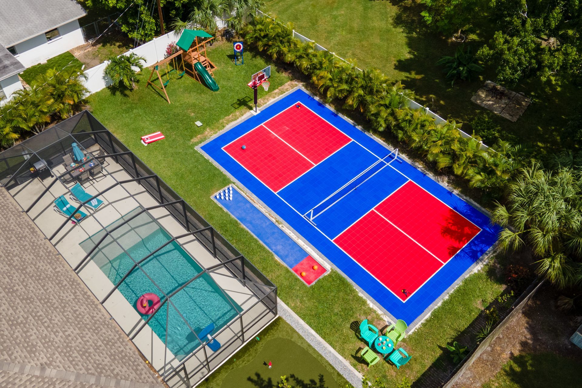 Aerial view of a backyard with a red and blue pickleball court, pool, and a play structure.