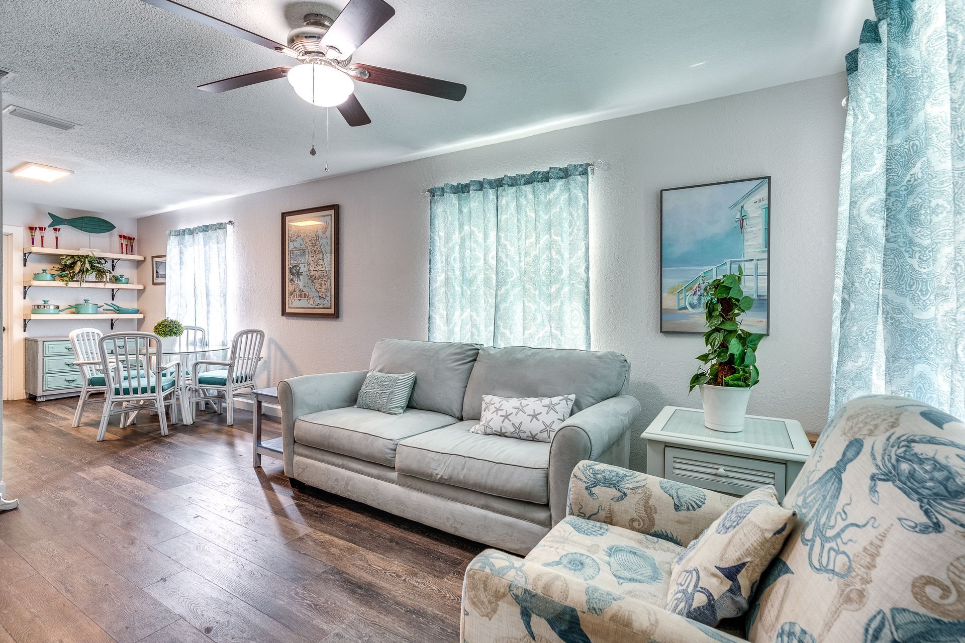Living room with beach theme, including a sofa, armchair, dining table, and ocean-themed decor.