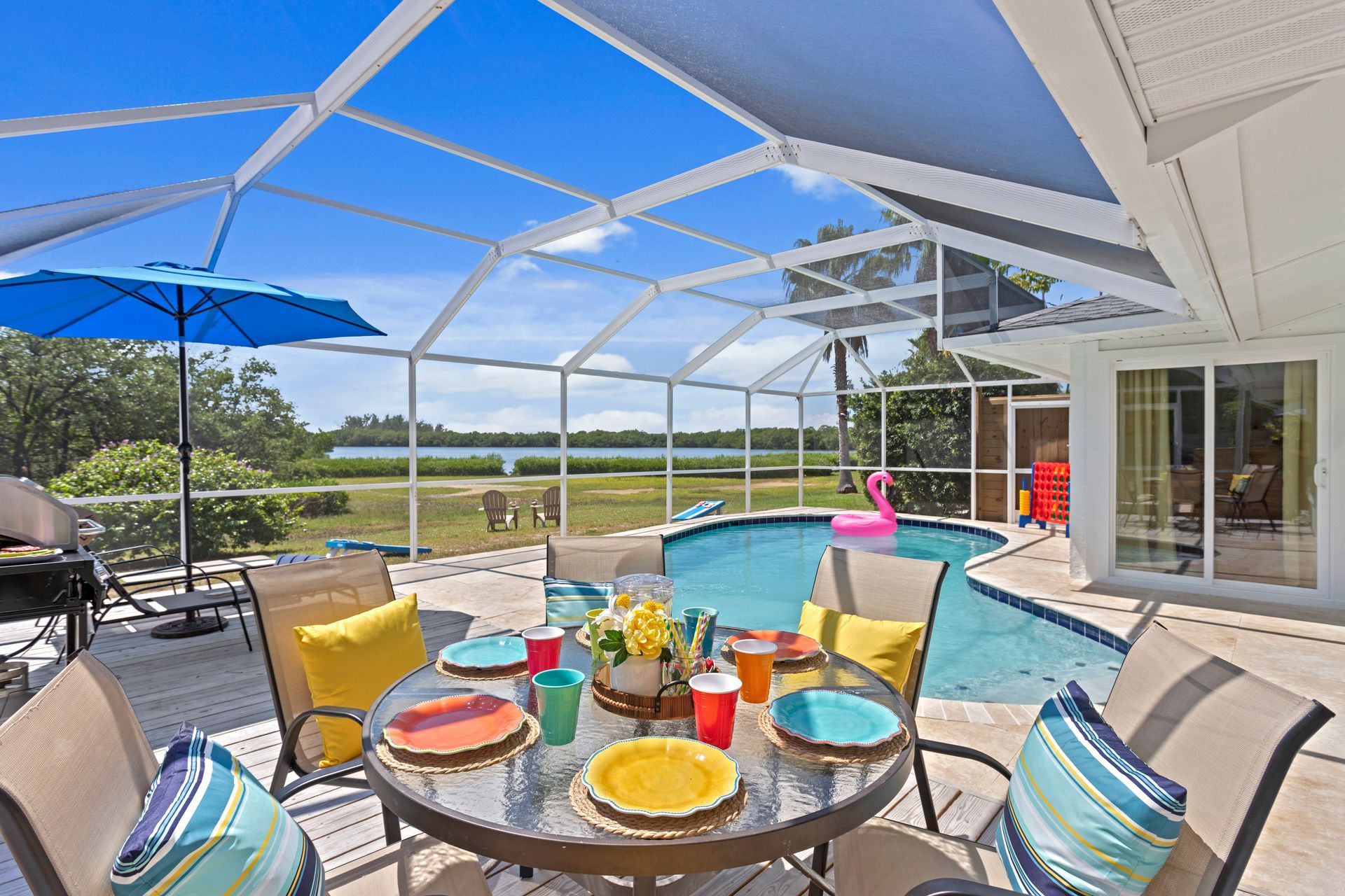 Outdoor patio with table set for dining, pool, and lake view under screened enclosure.