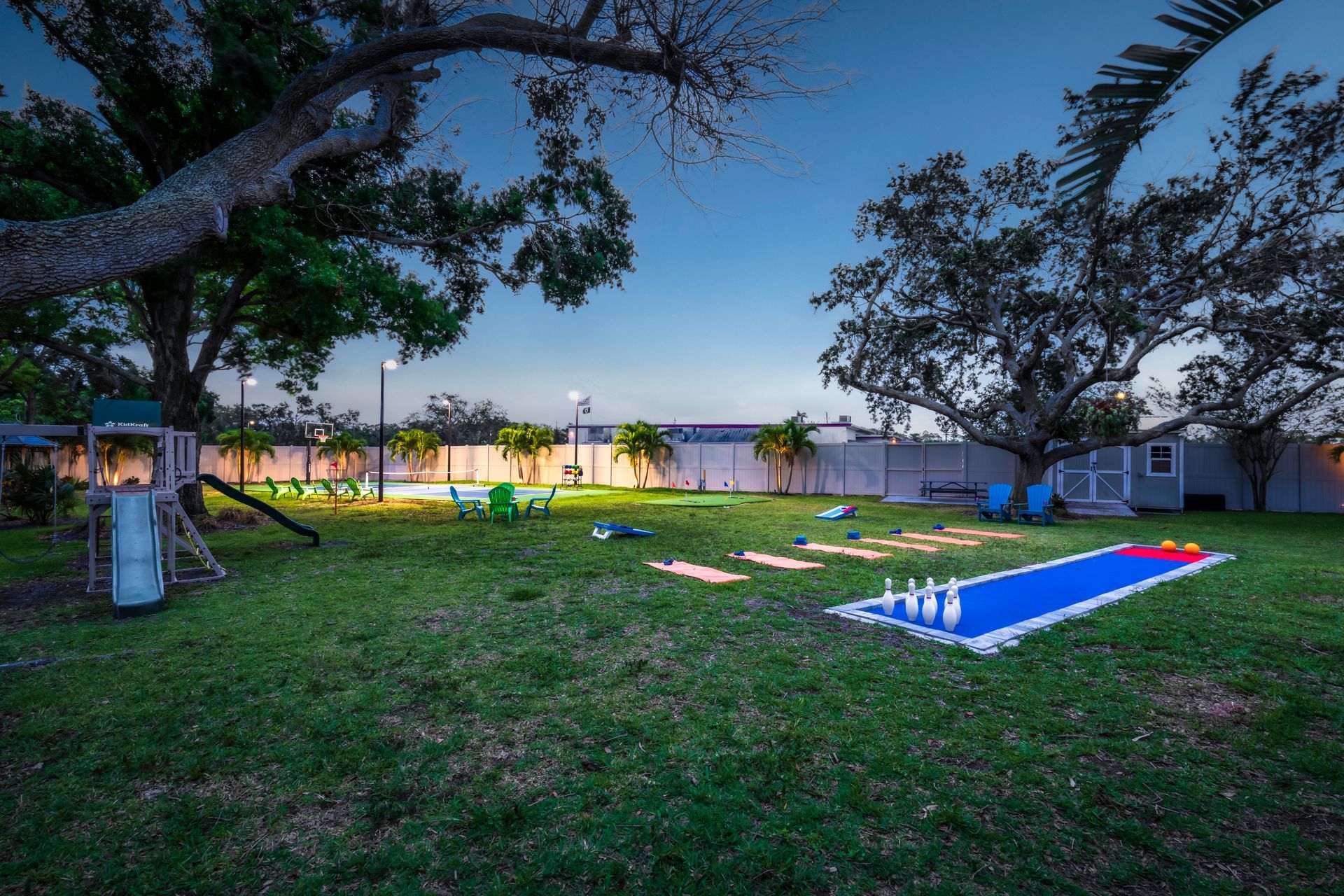 Backyard with lawn bowling, playground, and trees under a twilight sky.