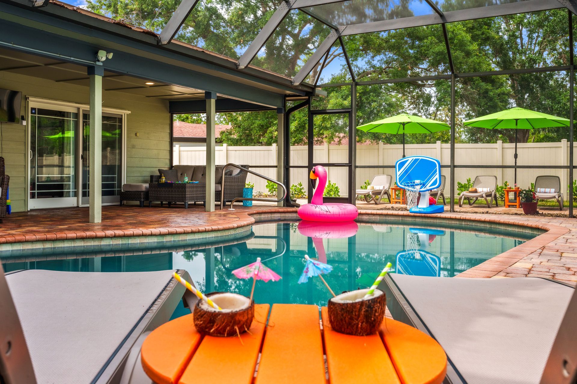 Poolside scene with coconut drinks on an orange table. The pool has floats.