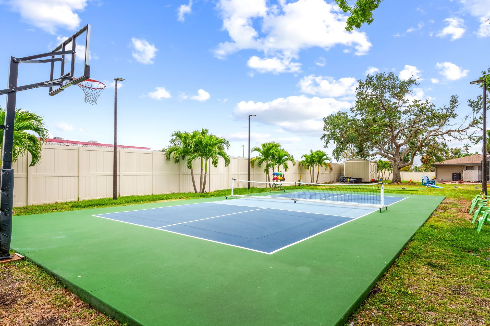 Basketball court with blue and green surface, hoops, and palm trees under a blue sky.