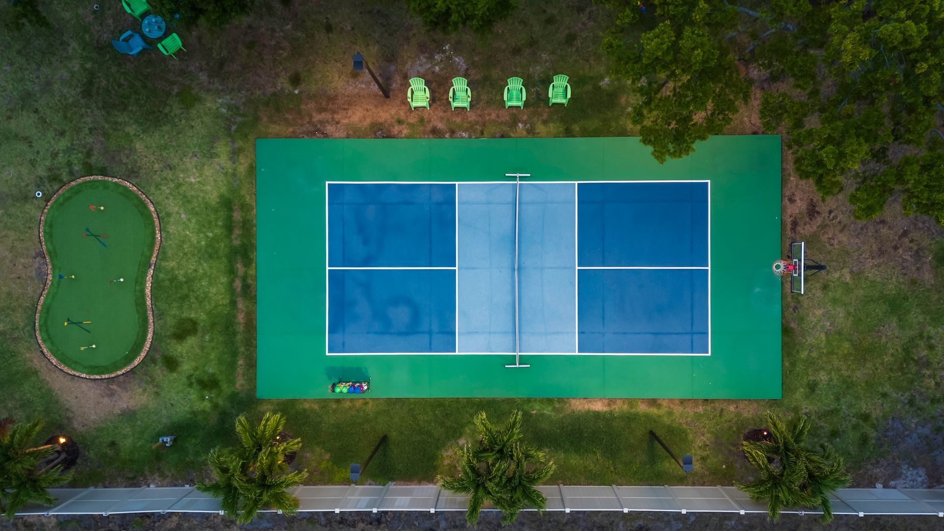 Aerial view: Blue and green pickleball court with mini-golf course and chairs on grass.