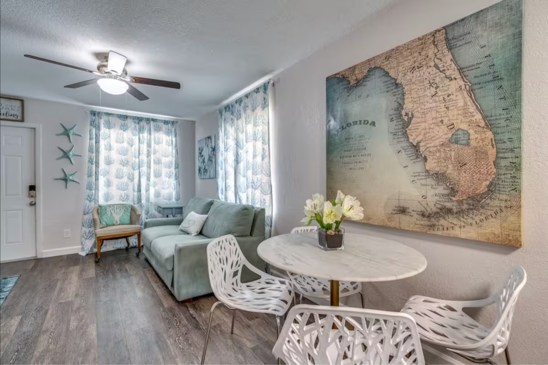 Cozy living room with turquoise couch, marble table, Florida map art, and white chairs.