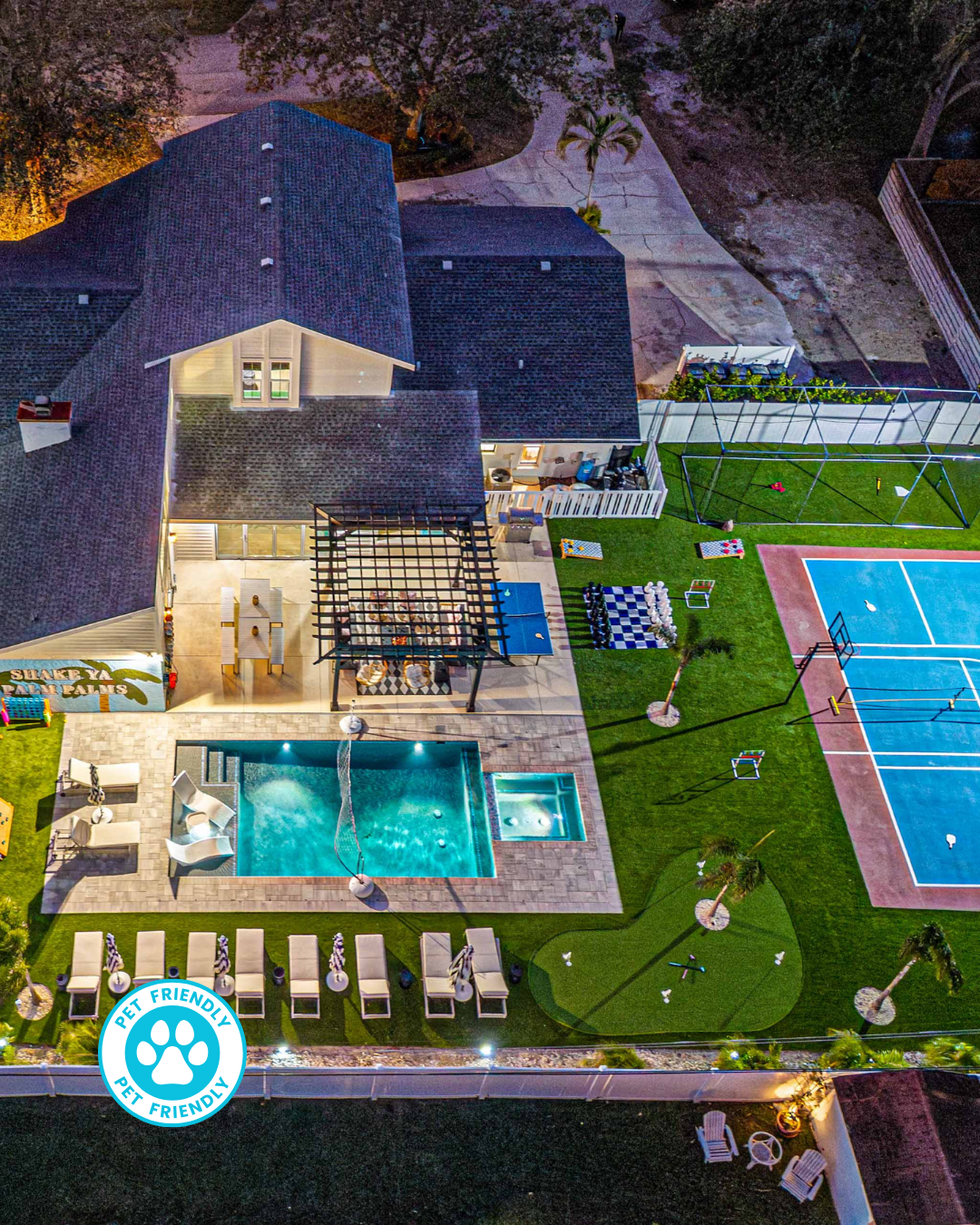 Aerial view of a backyard with a rectangular pool, a shaded patio area with tables, and several striped umbrellas.