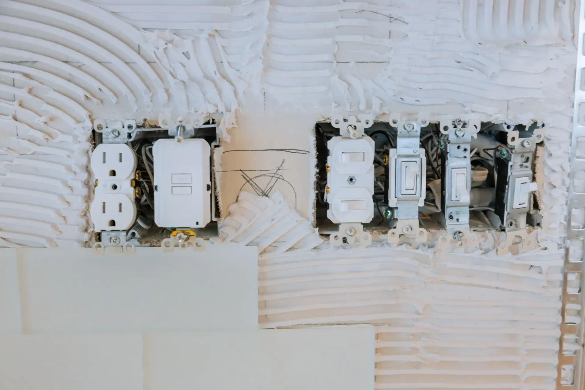 Tomas de corriente e interruptores eléctricos instalados en una pared con yeso blanco sin terminar.