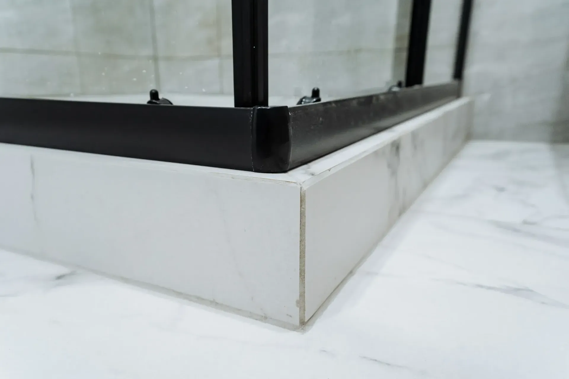 Mampara de ducha con marco negro sobre base imitación mármol blanco, en baño alicatado.