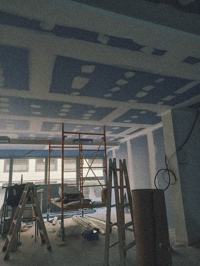 Interior en construcción: techo sin terminar con andamios y escaleras. Paredes azules, molduras blancas.