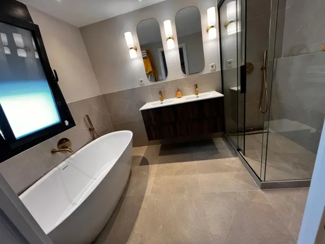 Baño moderno con bañera, tocador con espejos y ducha de cristal.