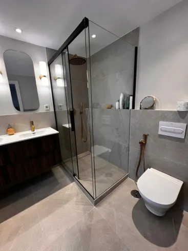 Baño moderno con ducha de cristal, inodoro flotante, tocador y azulejos de tono neutro.