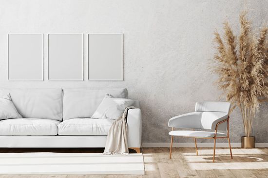 Weißes Wohnzimmer mit Sofa, Sessel, gerahmten Bildern und dekorativem Pampasgras.