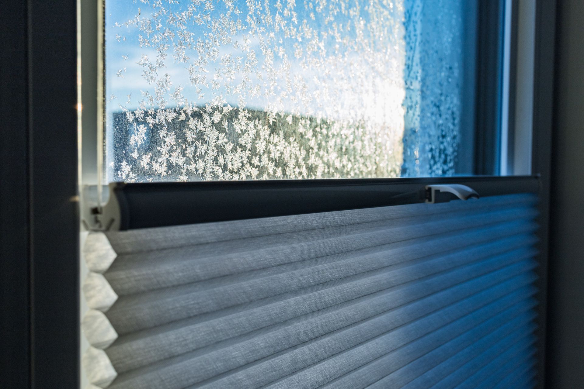 Frostiges Fenster mit teilweise geschlossenem Plissee.