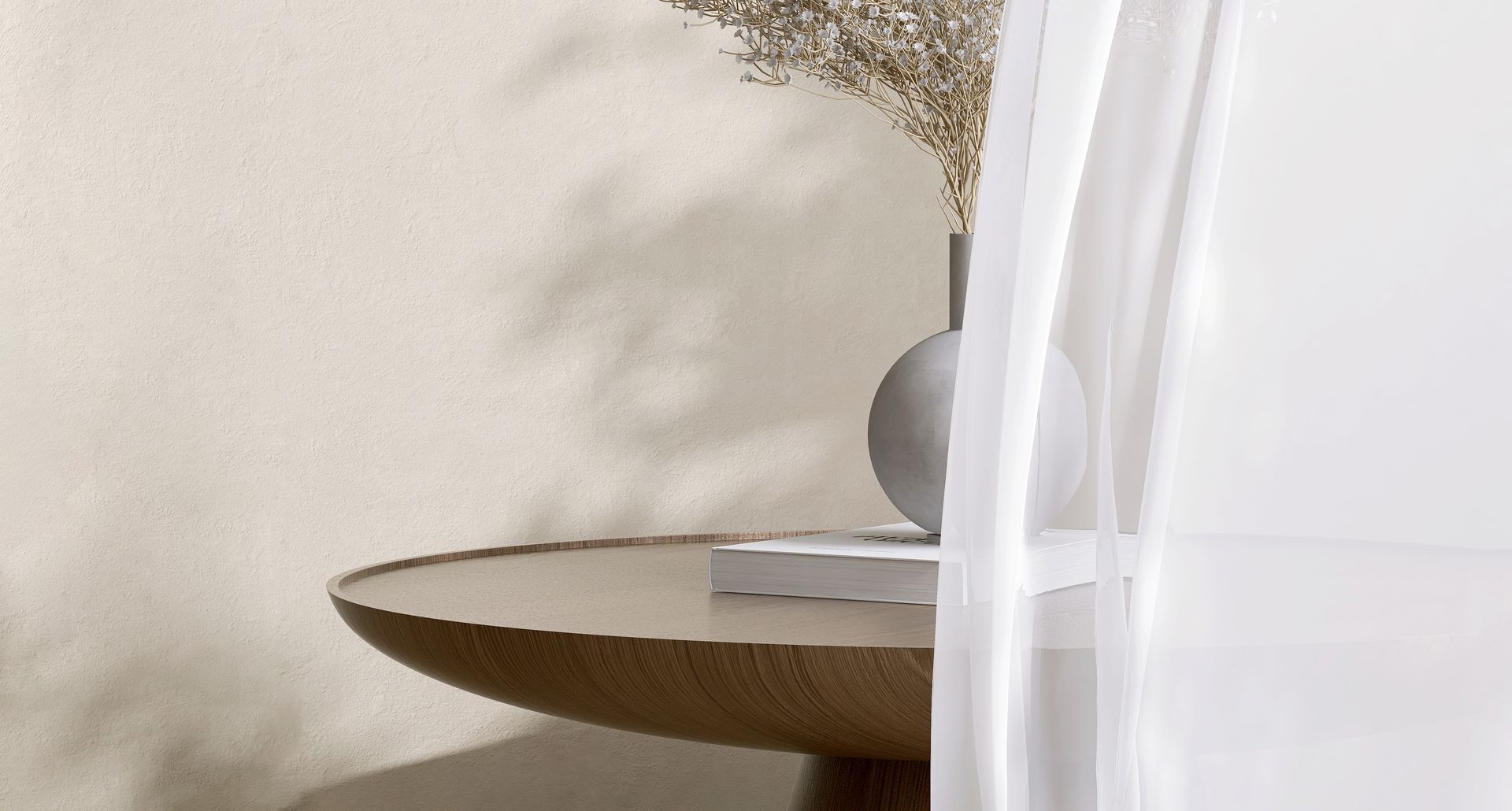 Ein runder Holztisch mit einer Vase mit Trockenblumen; im Vordergrund ein durchsichtiger weißer Vorhang, neutraler Hintergrund.