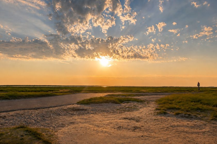 Sonnenuntergang über einem schneebedeckten Strand mit Dünengras und ruhigen Wellen am Horizont
