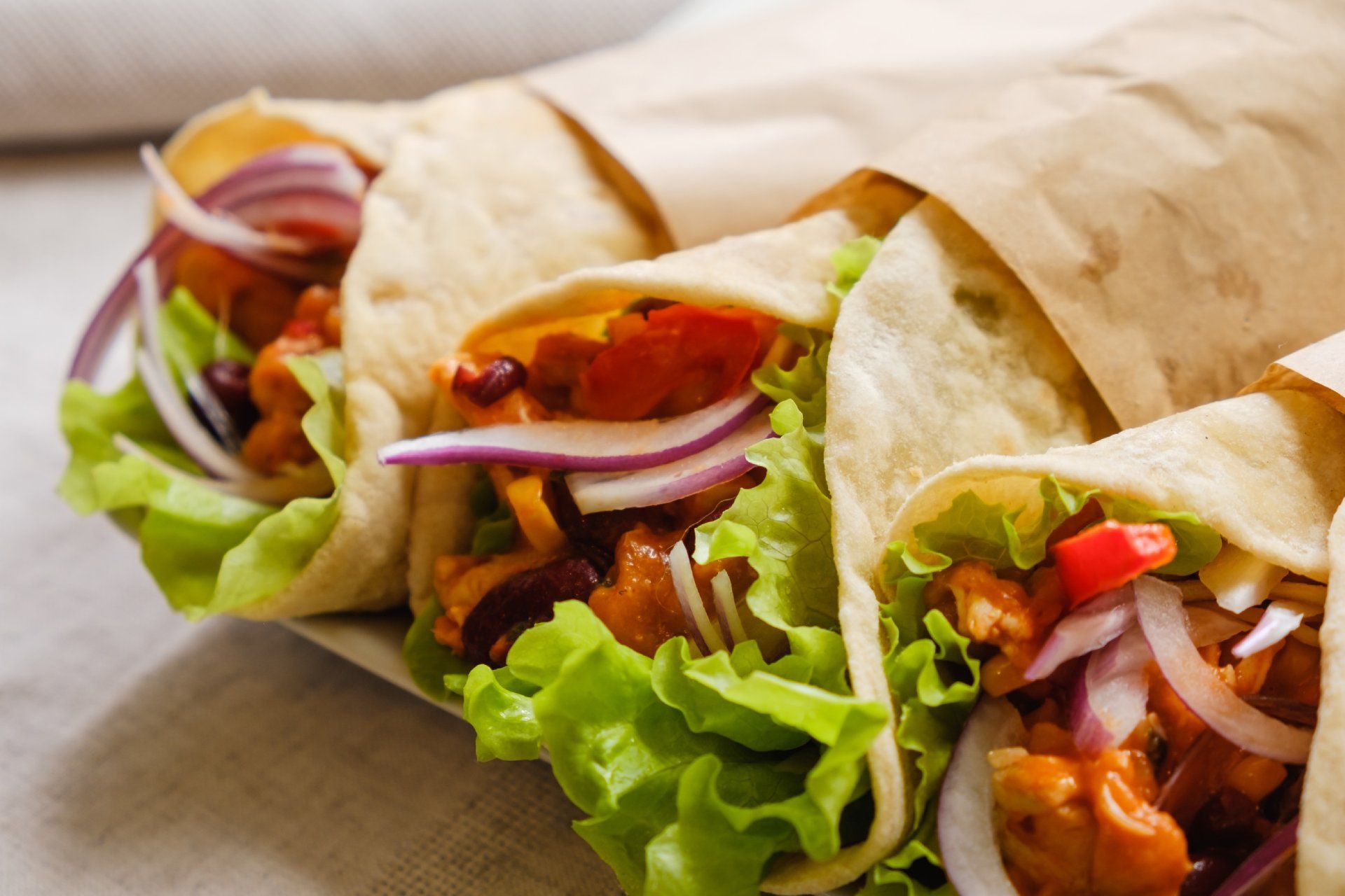 Kebabs envueltos en papel marrón, rellenos de lechuga, cebolla roja y carne.