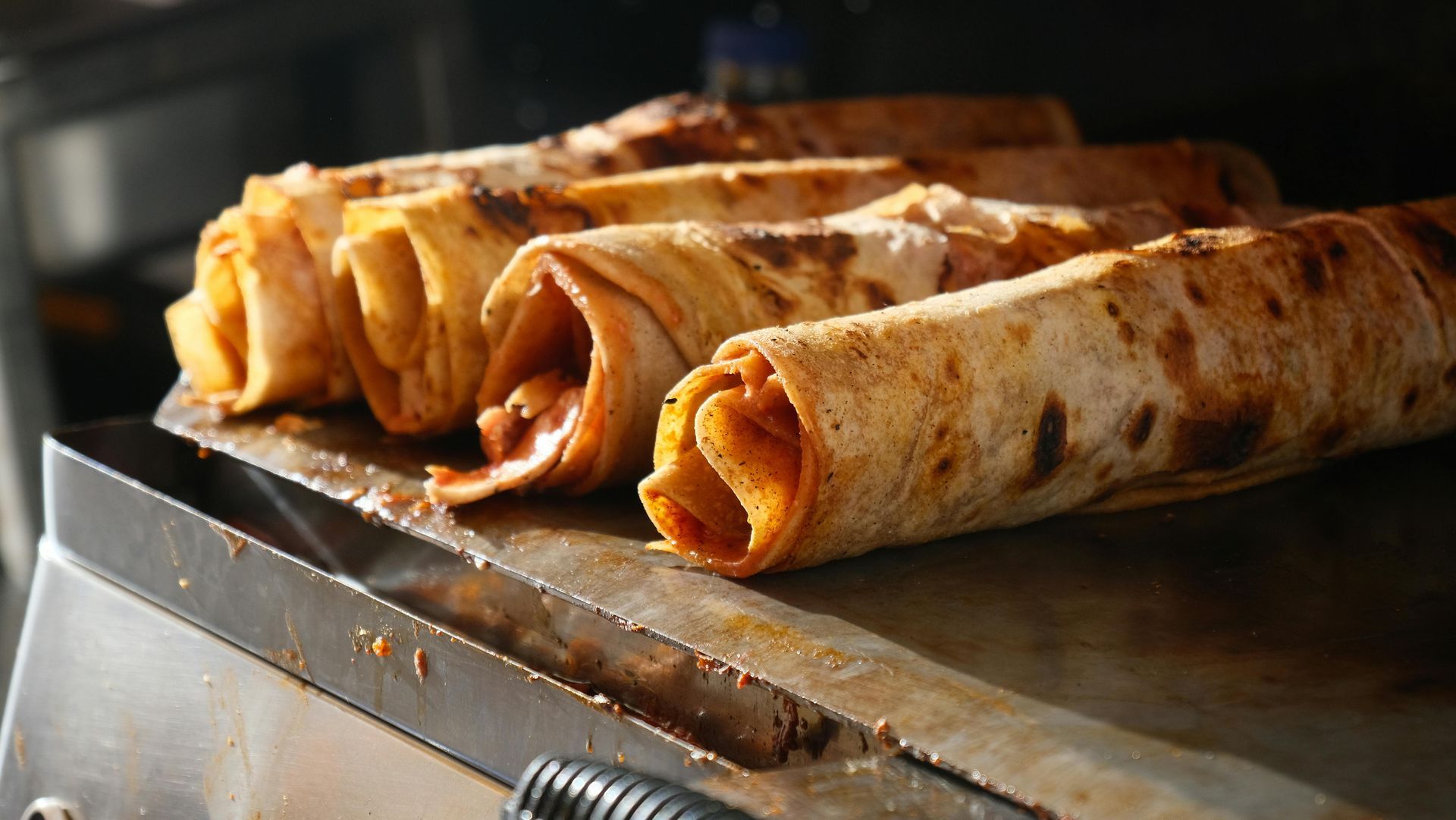 Tortillas rellenas y enrolladas, sobre una parrilla, listas para servir.